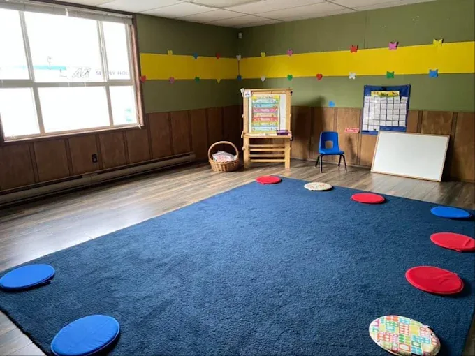 A large blue carpet ringed with round red and blue sitting cushions, an easel and a whiteboard.