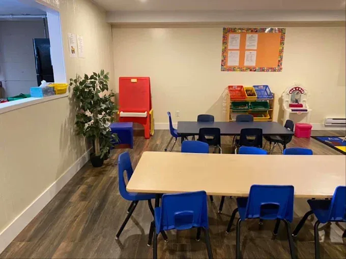 Child-sized tables with blue chairs, a red easel, a plant and labelled toy bins.